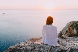 donna seduta su una scogliera che guarda il tramonto sul mare