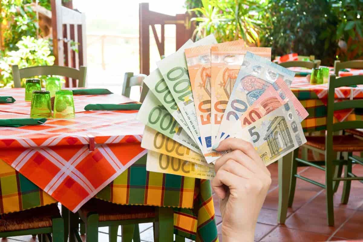 tavoli ristorante e mano con banconote euro